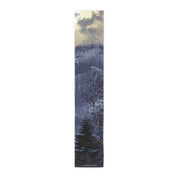 Dark pine tree in front of a hazy mountain range under a cloudy sky.