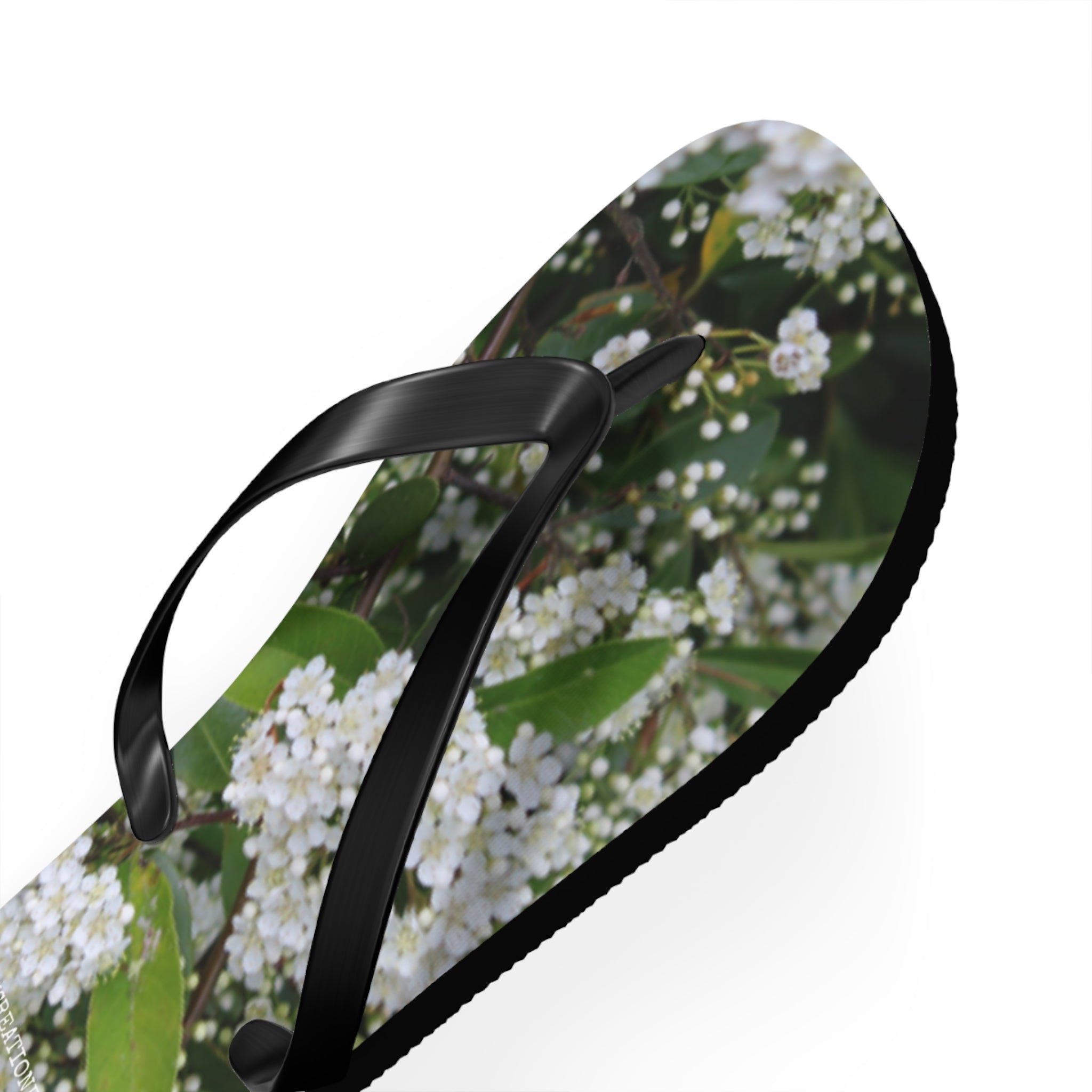 White floral pattern on flip-flop with black straps, on white background.